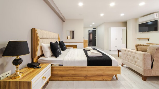 Una habitación de hotel moderna con una cama de madera, mesita de noche con lámpara, un sofá y un televisor fijado a la pared.
