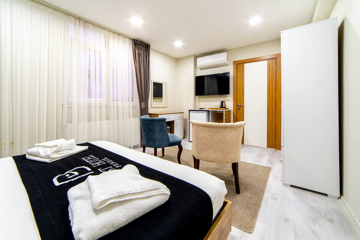 A hotel room with a bed, a desk, a chair, a television, and a refrigerator.