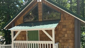 Eine kleine Holzhütte mit einer grünen Tür, einer weißen Veranda und einem Metallmülleimer.