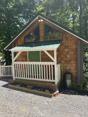 A small wooden cabin with a green door, a white porch, and a metal trash can.