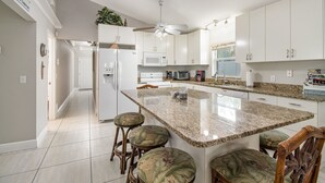 Una cocina moderna con armarios blancos, una isla de granito y taburetes de bar.