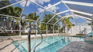 Piscina al aire libre con zona cubierta, rodeada de palmeras y cielo despejado.