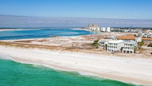 Une zone côtière comprenant une plage, une jetée et plusieurs bâtiments, dont une grande maison blanche à étages et dotée de balcons.