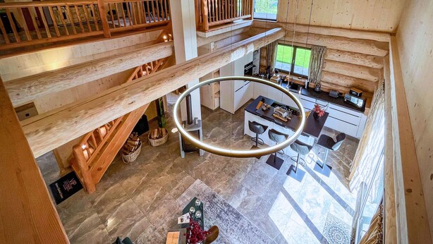 Un intérieur spacieux de style loft, avec un plafond haut, des poutres en bois, une mezzanine, un luminaire circulaire et un coin cuisine.
