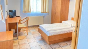 A bedroom with a bed, a desk with a computer, a chair, a wardrobe, and a window with curtains. - Single room (Pulheim)