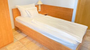 A single bed with white bedding, a wooden headboard, a nightstand with a lamp, and a framed picture on the wall. - Single room (Pulheim)