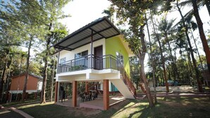 Edifici de dues plantes amb un balcó, envoltat d'arbres.