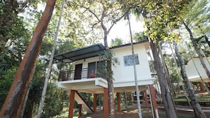 Una casa d'arbriol amb un balcó, envoltada d'arbres i vegetació.