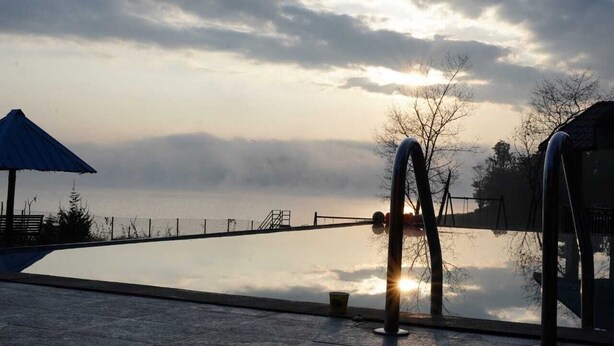 Una piscina amb vistes al capvespre sobre una extensió d'aigua, envoltada per una tanca i alguns arbres.