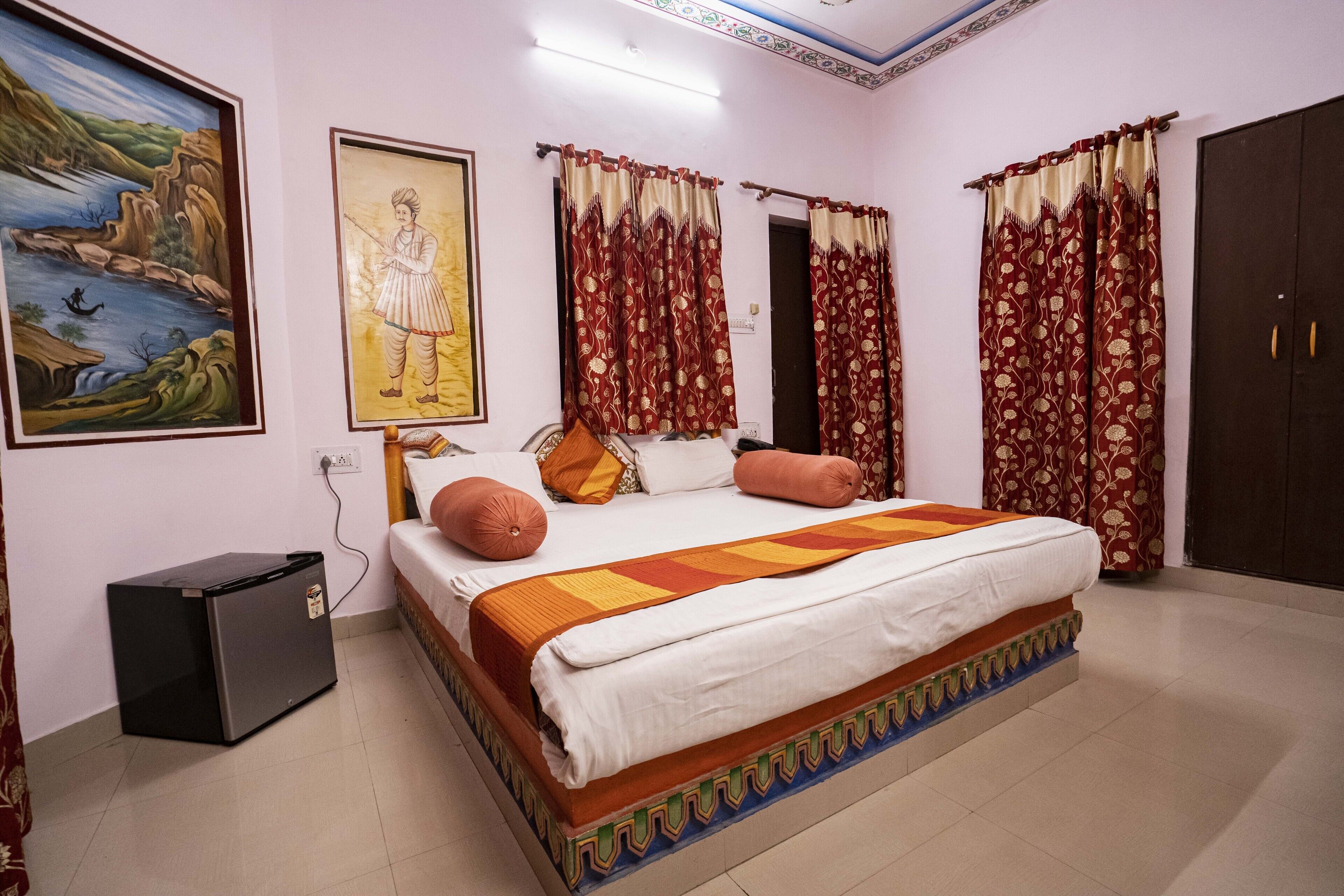 A bedroom with a bed, curtains, a wardrobe, and a small refrigerator.