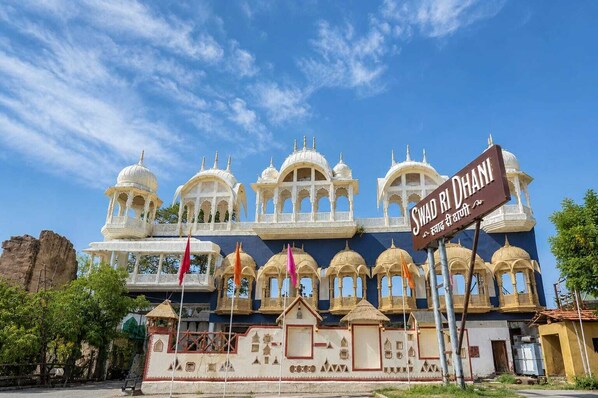 A large, ornate building with multiple domes and arches, a sign reading 'Swad R Dhani,' and a flagpole with flags.