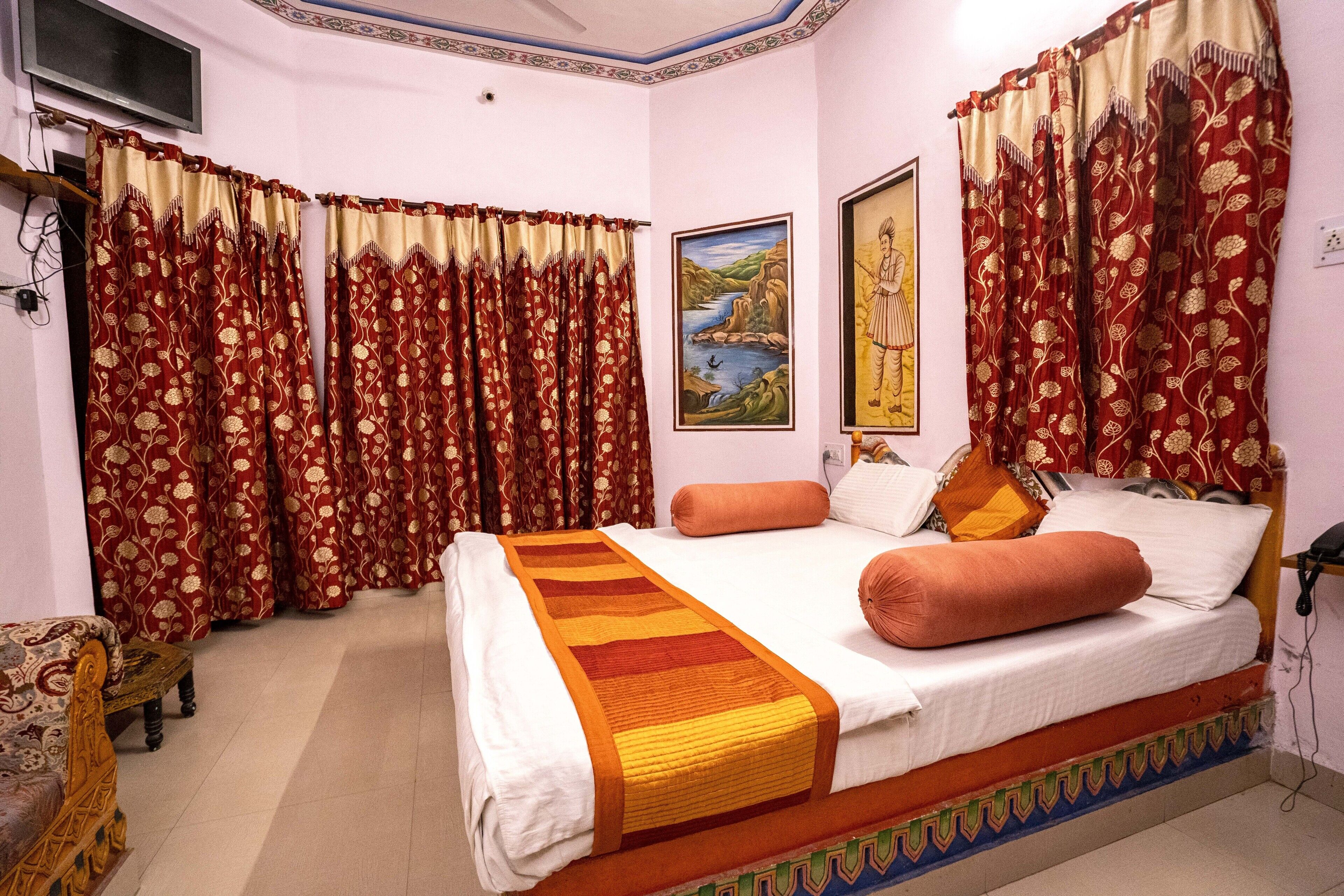 Une chambre avec un grand lit, des rideaux rouges, un tableau et un téléviseur accroché au mur.