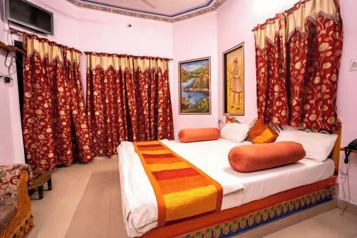 A bedroom with a bed, curtains, a painting, and a television.