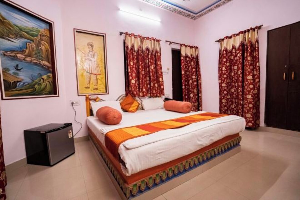 A bedroom with a bed, curtains, a painting, and a wardrobe.