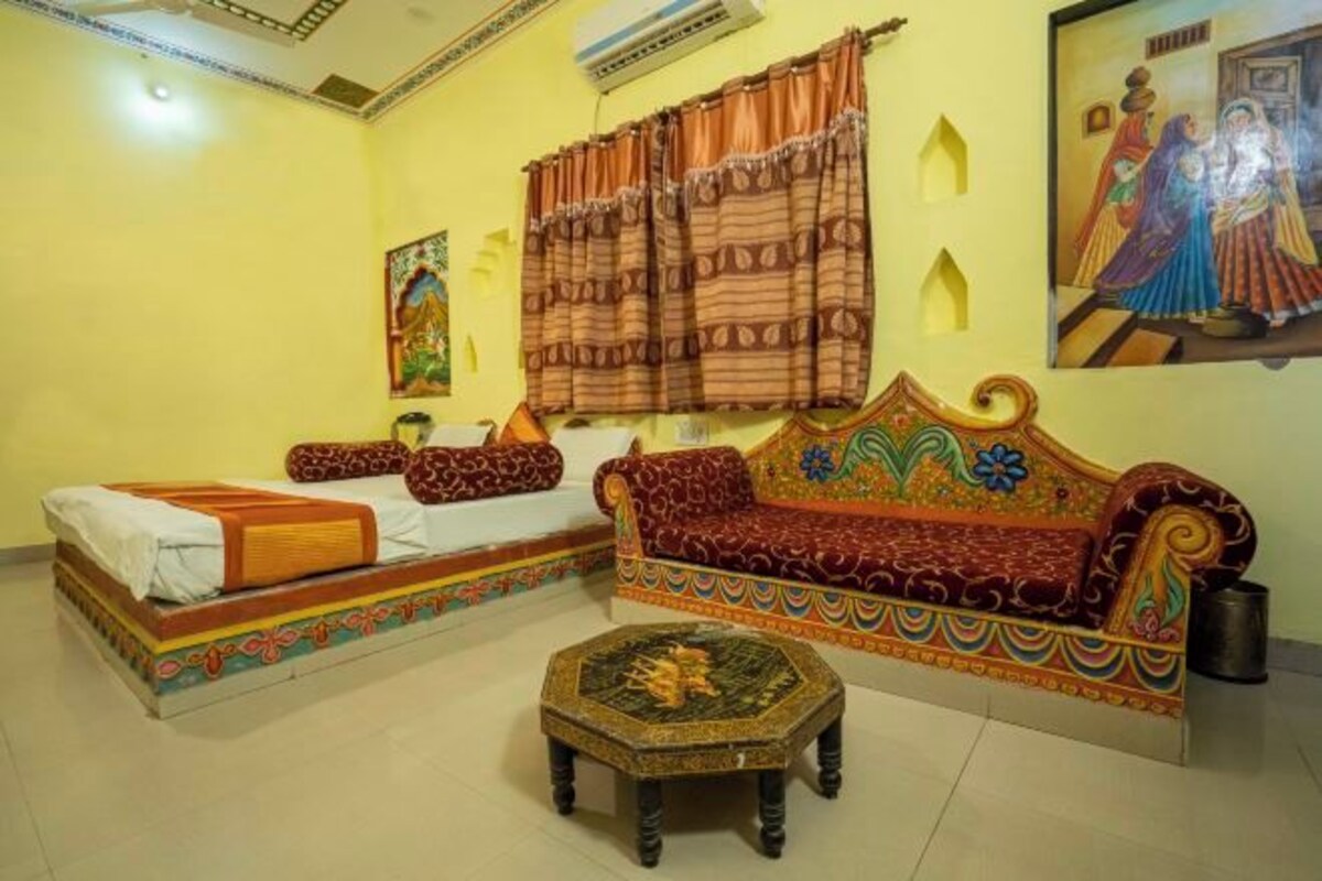 A room with a bed, sofa, and ottoman, with colorful patterns and artwork on the walls.