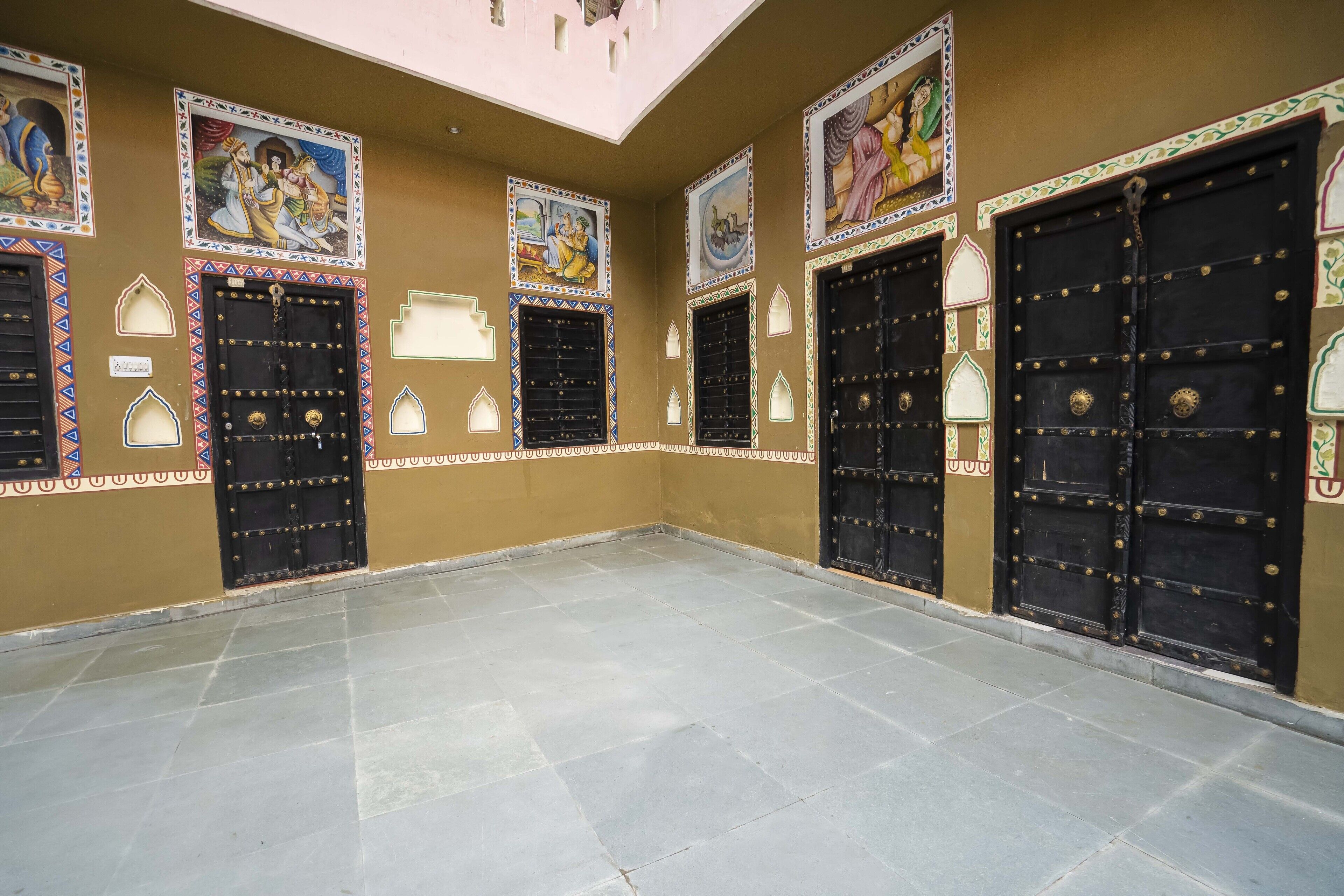 A spacious room with large black doors, decorative wall paintings, and tiled flooring.