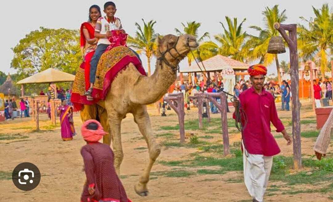 A camel with riders, a person walking, and a crowd in a rural setting.