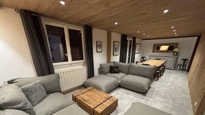 Una sala de estar moderna con sofás grises, una mesa de centro de madera y un comedor al fondo.