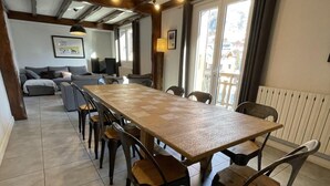 Un comedor amplio con una larga mesa de madera y sillas, un sofá y un televisor al fondo.