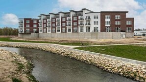 A multi-story residential building with a modern architectural design, featuring a mix of brick and white facades, and a landscaped area with a water feature in front.