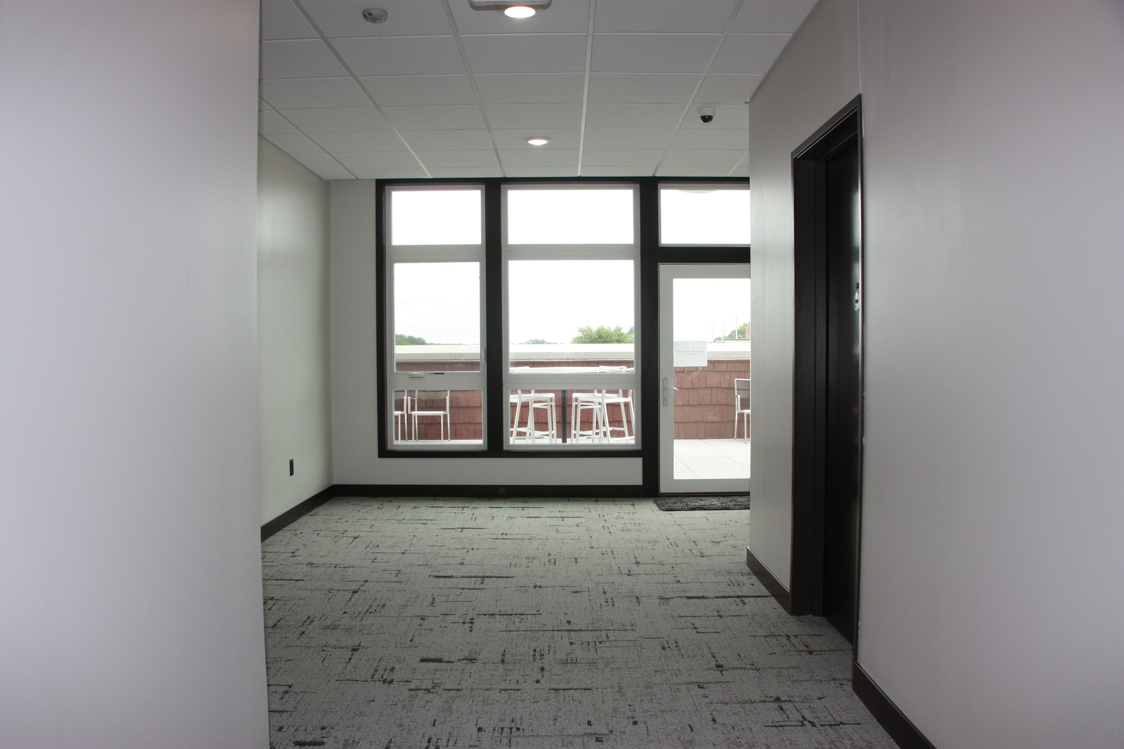 A hallway with large windows, a door, and a patterned carpet.