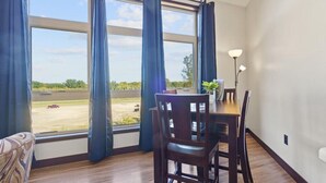 A dining area with a table and chairs, large windows with curtains, and a view of a parking lot.