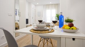 A modern dining area with a white table set for two, including wine glasses, a blue water bottle, and a bowl of fruit.