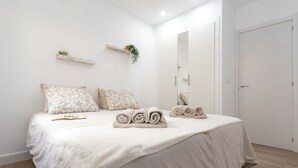 A bedroom with a large bed, a bedside table with a book and glasses, a mirror, and a door.