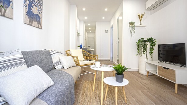 A modern living room with a grey sofa, a small round table, a TV, and a wicker chair.