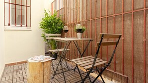 A small outdoor seating area with a wooden table and chairs, a potted plant, and a bamboo fence.