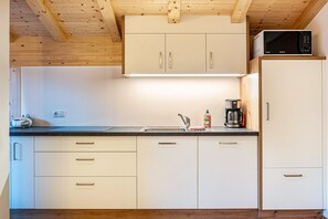 A kitchen with wooden ceiling beams, white cabinets, a microwave, a coffee maker, and a radio.