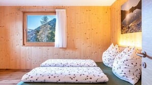 Une pièce aux murs lambrissés, avec un lit, une fenêtre donnant sur une montagne et un tableau accroché au mur.