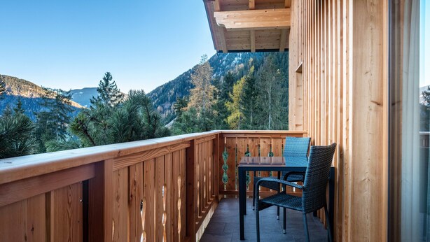 Un balcon en bois, agrémenté d’une table et de chaises, qui offre une vue sur un paysage montagneux.