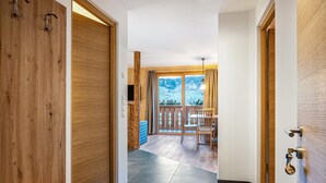 Un couloir avec des portes en bois, un banc, un coin repas avec des chaises et une table, et une vue sur un paysage enneigé par de grandes fenêtres.