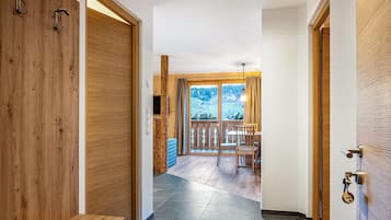 A hallway with wooden doors, a bench, a dining area with chairs and a table, and a view of a snowy landscape through large windows.