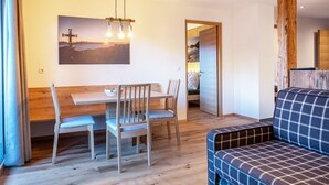 Un coin repas avec une table et des chaises en bois, un banc, un canapé et un tableau représentant un coucher de soleil accroché au mur.