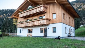 Une maison en bois à deux étages, dotée d’un balcon, d’un banc et d’un chien.