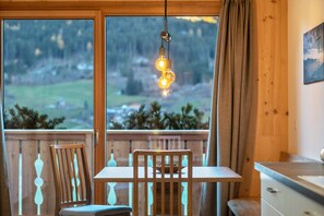 A wooden-framed room with a table and chairs, a hanging light fixture, and a view of a forested landscape through large windows. - Holiday Apartment Mittnackerhof Ringelblume with Mountain View, Balcony & Wi-Fi (Sarentino)