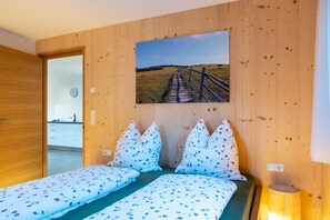 A bedroom with two beds, wooden walls, a clock, and a painting of a pathway. - Holiday Apartment Mittnackerhof Ringelblume with Mountain View, Balcony & Wi-Fi (Sarentino)