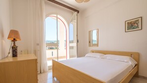 A bedroom with a wooden bed, a bedside table with a lamp, a mirror, and a view through a glass door. - Villa "Delle Pomelie" with Private Garden, Balconies, and Wi-Fi (Furnari)