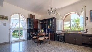 A kitchen with a dining table, chairs, a chandelier, and a large window with a view of palm trees. - Villa "Delle Pomelie" with Private Garden, Balconies, and Wi-Fi (Furnari)
