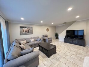 A modern living room with a sectional sofa, a dark coffee table, a TV, and a staircase leading to another level.