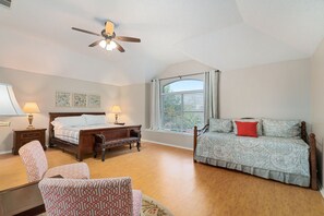 A bedroom with a bed, a chair, a desk, a ceiling fan, and a window with curtains.