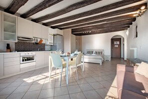 Une cuisine moderne avec des meubles blancs, un coin repas comprenant une table et des chaises, un canapé et un plafond en bois.