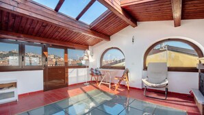 A room with a glass floor, wooden ceiling beams, large windows, and a view of a cityscape.