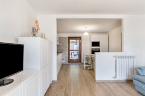 A modern kitchen with white cabinets, a flat-screen TV, a refrigerator, and a dining area with a table and chairs. - Pet-Friendly Apartment Edik with Mountain View & Terrace (San Sebastiano)