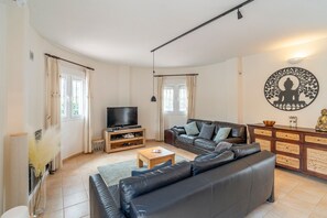 Uma sala de estar com sofá, mesa de centro, TV em um móvel e um objeto decorativo na parede.