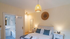 Un dormitorio con cama, mesitas de noche, lámpara colgante, espejo y una puerta.