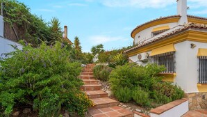 Un jardín con una escalera de piedra que conduce a un edificio de fachada amarilla y pared blanca.