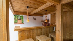 Interior de madera con techo de madera, ventana con vistas a follaje y una lámpara fijada a la pared.